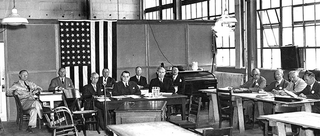 Commerce Department Inquiry, May 27, 1937. Seated at the small table in center are, left to right: R.W. Schroeder; Colonel South Trimble, Jr. (Chairman); and Dennis Mulligan. Technical advisors seated at the large table behind them are, left to right: Commander Charles E. Rosendahl, USN; Gill R. Wilson; Colonel R.B. Lincoln, U.S. Army; Lieutenant Colonel C. de F. Chandler; and Colonel H.E. Hartney. Stated at right are, left to right: G.C. Lovening, Frederick Hoffman, Dr. Hugo Eckener and Ludwig Dürr.